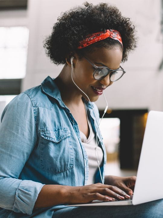 female on bench with laptop and headphones on learning