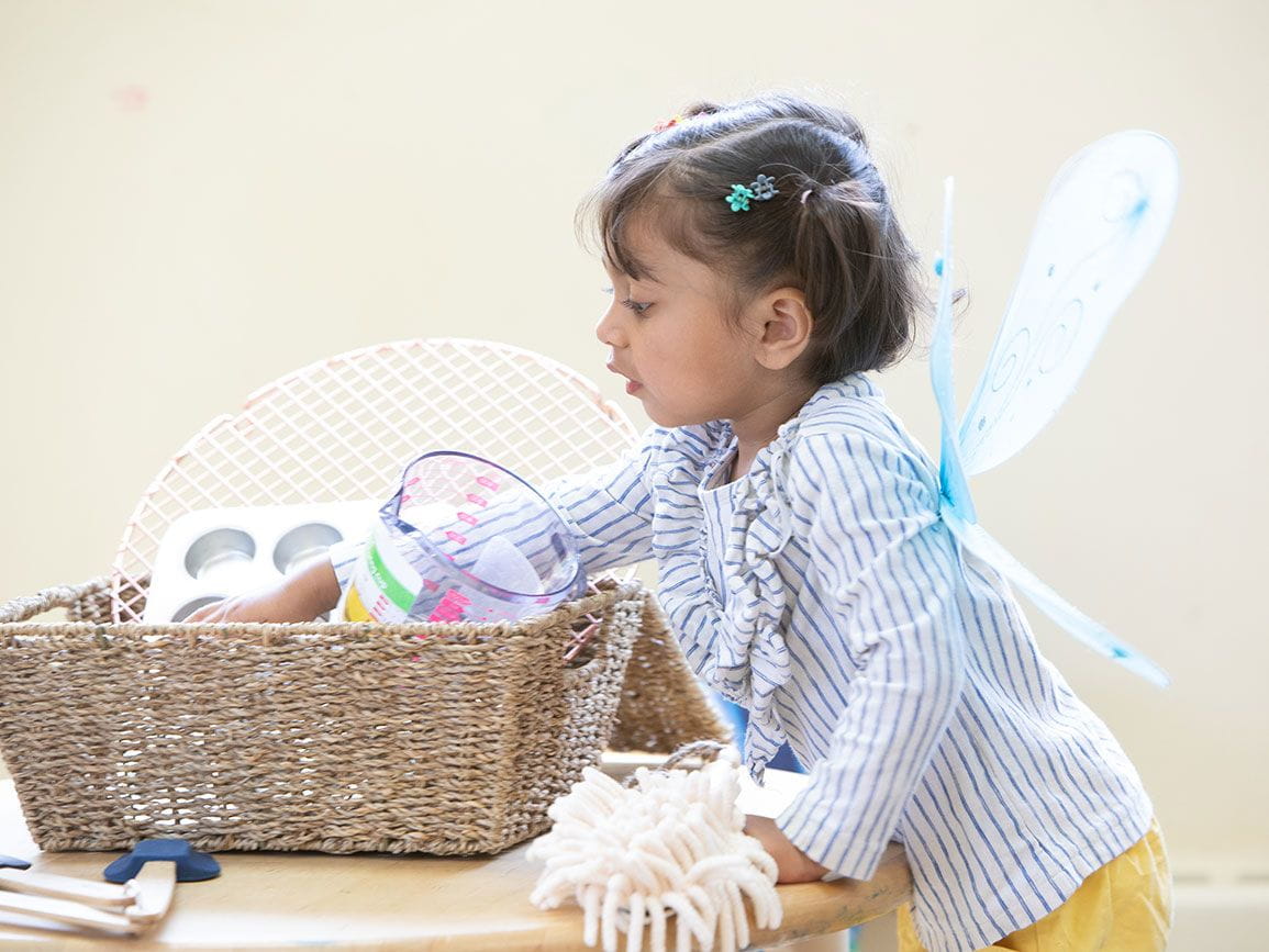 little girl with toy fairy wings looking in a basket