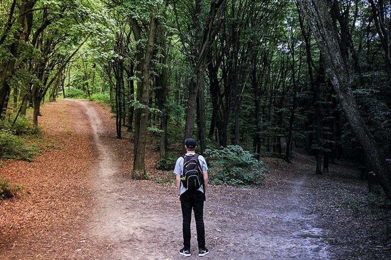 Young male standing before two divergent paths